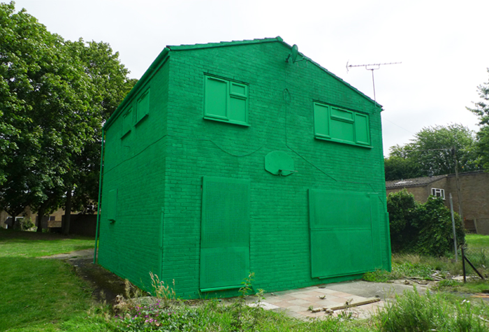 Small building painted entirely green in a field